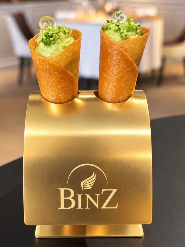 🍦 Le cornet végétal, fraîcheur en éveil du palais

🥦 Dans son cône croustillant, Julien Binz travaille le brocoli sous deux formes : cuit, en crème douce et enveloppante relevée de vinaigre de riz ; cru, fraîchement râpé, pour retrouver sa mâche, son caractère végétal et ses notes plus franches.

🍋 Quelques billes de yuzu viennent ponctuer la dégustation. Leur vivacité citronnée répond au brocoli et construit l’acidité en deux temps : fine et diffuse avec le vinaigre de riz, plus éclatante avec le yuzu.

🍦 La forme fait le reste : celle d’un petit cornet que l’on saisit avec les doigts et qui évoque immédiatement une glace. Le clin d’œil s’arrête pourtant à l’apparence : la bouchée, elle, est végétale, vive et acidulée.

✨ Ce cône se décline au fil des saisons et des inspirations du chef, en conservant le même geste : le saisir avec les doigts pour entrer dans le menu de manière volontairement décomplexée.

💛 Il est présenté dans un socle en laiton doré dessiné par le père de Julien Binz, un objet créé spécialement pour accompagner cette signature introductive.

Une bouchée en trompe-l’œil élégante qui donne le ton de l’expérience chez Julien Binz.

📸 Texte : Sandrine Kauffer-Binz

#JulienBinz #RestaurantJulienBinz #Ammerschwihr #Alsace