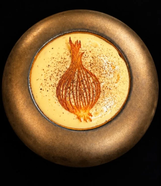 🧅☕ L’OIGNON ET LE CAFÉ, L’AUDACE de JULIEN BINZ 

🧅Il transforme un ingrédient du quotidien en une création gastronomique pleine de caractère.

🧅 L’oignon devient la vedette ✨✨

🔥 Pourquoi l’associer le café ? 
Parce qu’ils partagent une belle complicité aromatique !

👉La cuisson révèle les sucres naturels de l’oignon, développe sa douceur caramélisée et concentre ses saveurs.

☕ Le café, avec ses notes torréfiées, apporte profondeur, intensité et une pointe d’amertume qui équilibre cette gourmandise.

✨ Le premier plaisir est visuel. Une délicate tuile croustillante, finement dessinée en forme d’oignon, signe cette création avec élégance.

✨Une véritable dentelle dorée qui invite à découvrir ce qu’elle dissimule.

✨  Sous cette tuile craquante, un siphon aérien d’oignon caramélisé au café enveloppe une succession de textures gourmandes : oignons fondants, frits et jus d’oignon caramélisé au jus de veau, croûtons à l’ail, herbes et au vinaigre balsamique.

🤎 La poudre de café intensifie les notes torréfiées tandis que le jus apporte puissance et longueur en bouche.
👉Le croustillant rencontre le soyeux, la douceur répond à l’amertume, les saveurs se prolongent et s’enrichissent.

👉L’oignon possède cette capacité remarquable à donner du corps et de la profondeur aux préparations.
Riche en composés soufrés et en antioxydants, il possède aussi de belles qualités nutritionnelles.

📞 Réservations : 03 89 47 16 05
🔗 Lien de réservation en story

✍️📸 Texte et photo : Sandrine Kauffer-Binz